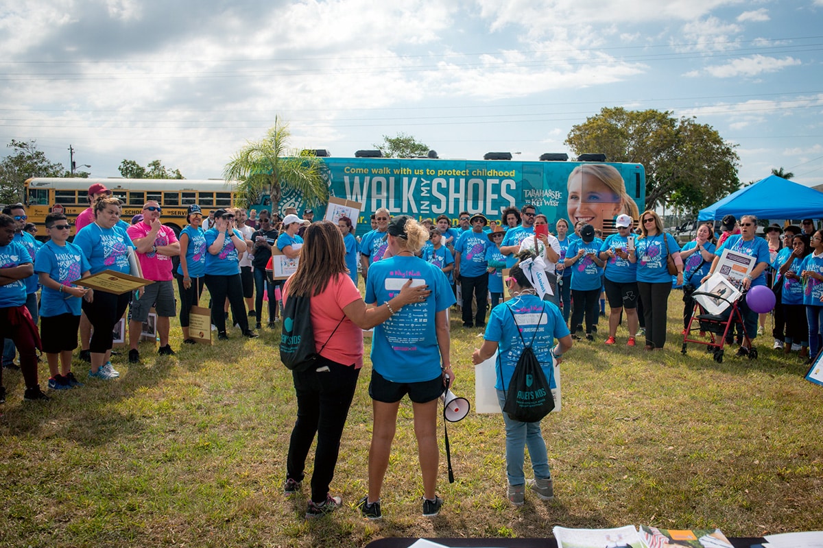 Group announcement for Lauren's Kids walk in front of a group and the wrapped bus